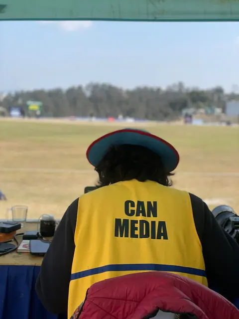 A sports photographer in a CAN Media vest watching the field.