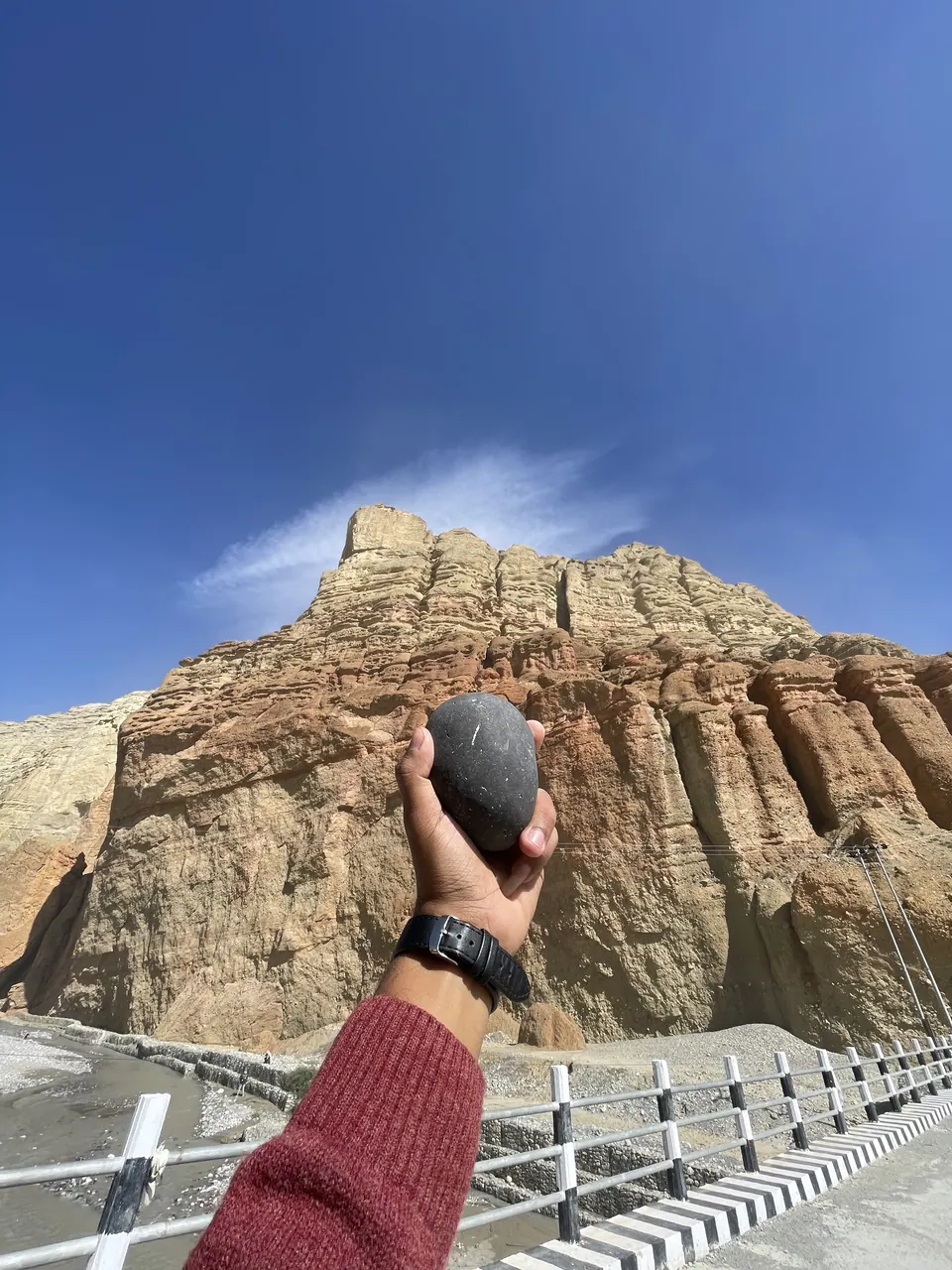 A hand reaching toward weathered high-altitude cliffs.