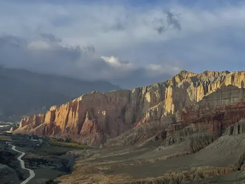 Sunlight striking banded cliffs above a mountain river.