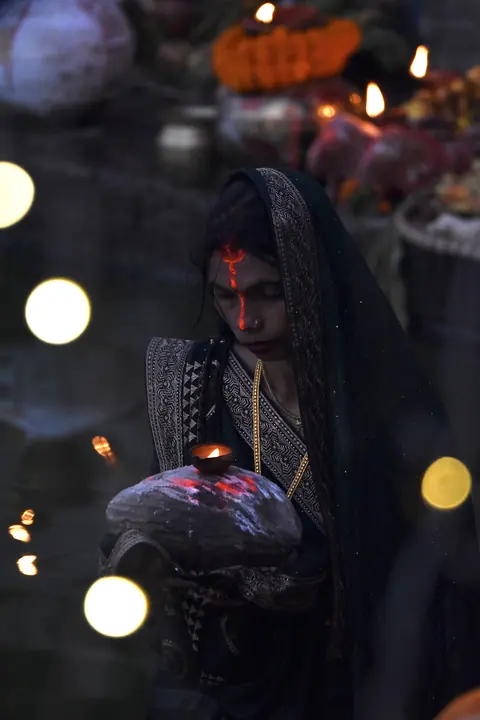 A woman in red holding an offering among evening lights.