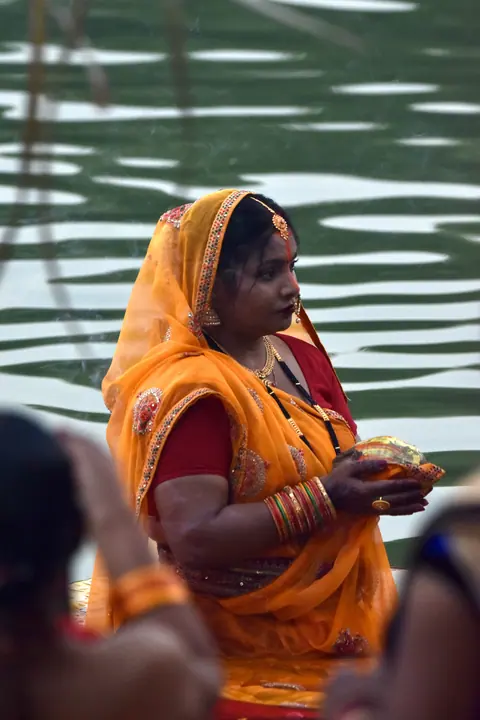 A woman carrying an offering beside rippling water.