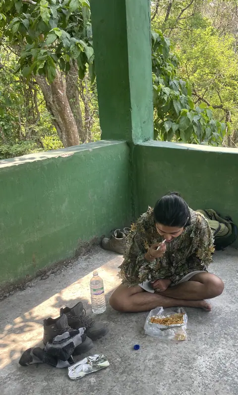 A traveller resting with a meal beside a green wall.