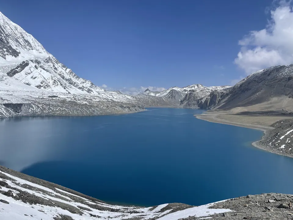 A deep blue high-altitude lake ringed by snow and rock.