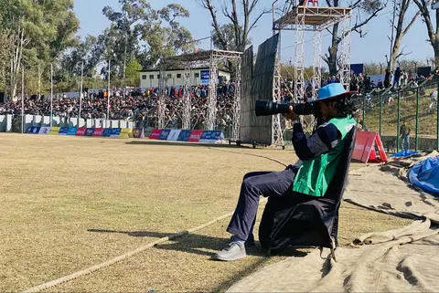 A photographer seated beside a cricket boundary.