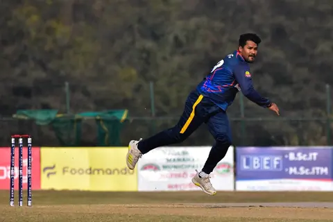 A fast bowler in motion on a cricket field.